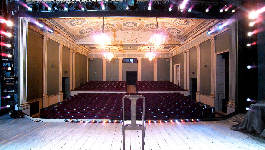 Gate Auditorium a chair sits in the middle of a brightly lit stage looking out onto hundreds of seats